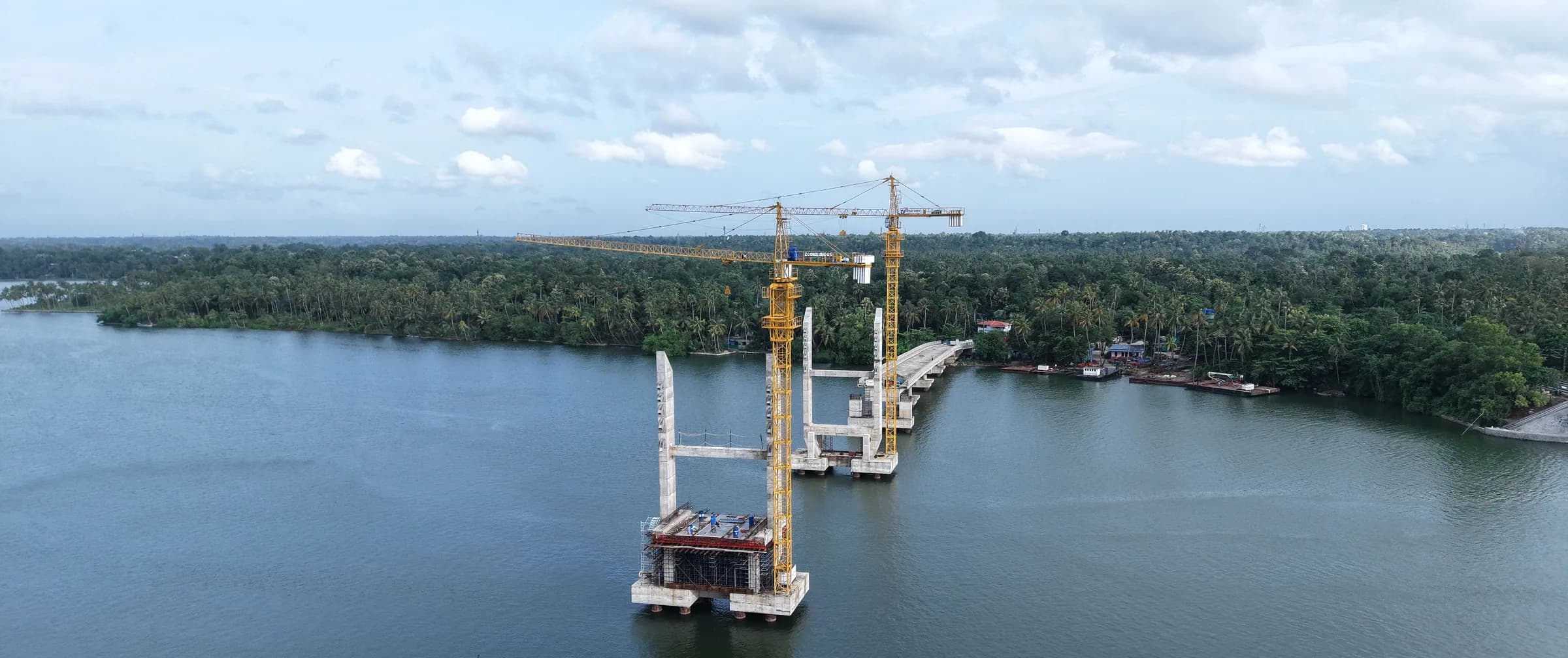 A bridge under construction over a river, seen from the air, with two tower cranes